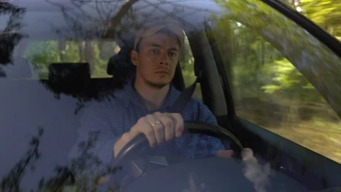 Young man looking around driving car along forest side on summer day. Stock Footage 113143631