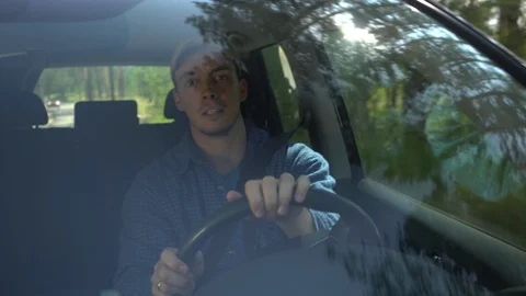 Young man looking around driving car along forest side on summer day and use Stock Footage 113144887