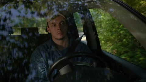 Young man looking around driving car along forest side on summer day. Stock Footage 113145592