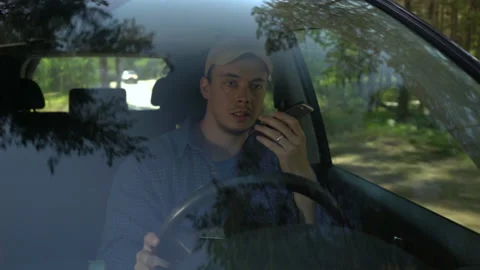 Young man looking around driving car along forest side on summer day and talking Stock Footage 142324063
