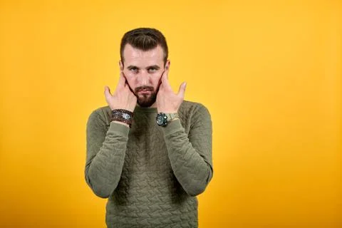 Young man looking at camera, keeping hand on beard wearing casual green clothes Stock Photos