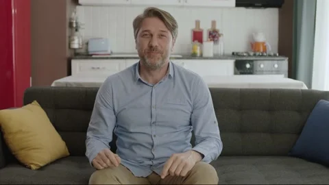 Young man looking at camera while sitting on sofa at home. Stock Footage 185563512