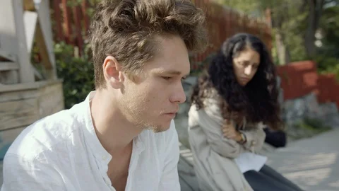 Young man looking concerned and thinking with his girlfriend in the background. Видео 115607469