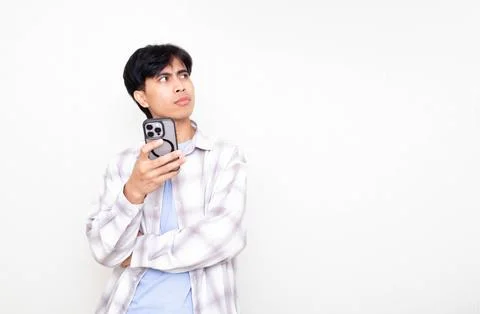 Young man looking confused while checking his smartphone, expressing doubt .. Stock Photos