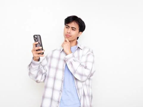 Young man looking confused while checking his smartphone, expressing doubt .. Stock Photos