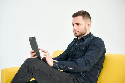 Young Man looking at digital tablet sitting on bright sofa Stock Photos