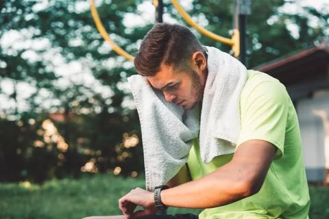 Young man looking down at his sports watch after his training, while wiping away Stock Photos