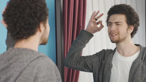 Young man looking at himself in the mirror but complaining about himself. Video stock 233028213