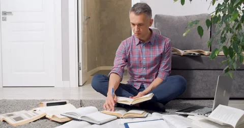 Young man looking for information in many books and textbooks and taking notes Stock Footage 149821696