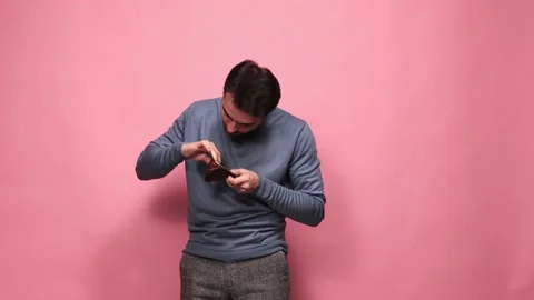 Young man looking inside empty wallet against pink studio background. Financial Stock Footage 234660786