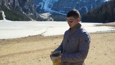 Young Man looking at map with lake and mountains on background 스톡 동영상 75789960