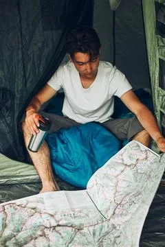 Young man looking at a map of mountain trails planning next trip on summer va Stock Photos