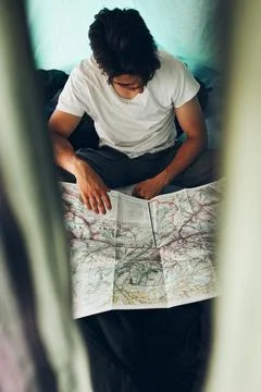 Young man looking at a map of mountain trails planning next trip on summer va Stock Photos