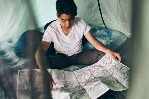 Young man looking at a map of mountain trails planning next trip on summer va Stock Photos