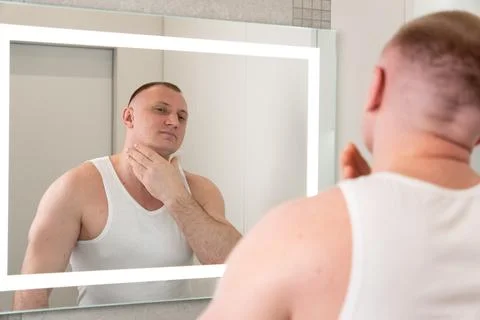Young man looking in mirror after shaving during morning grooming routine Фото