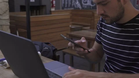 Young man looking at mobile with computer in outdoors bar Vidéo 153106489