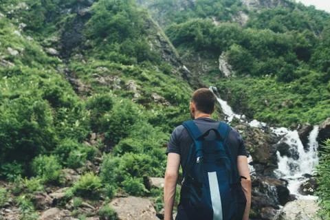 Young man looking at mountain stream in the forest admires nature. 写真素材