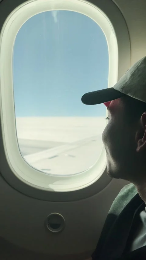 Young man looking out the airplane window contemplating the sky and clouds Video stock 319348428