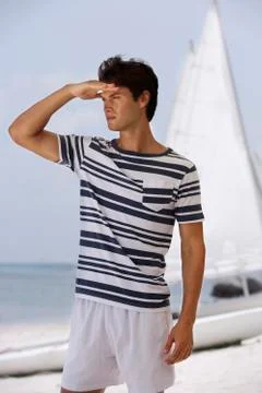 Young man looking out to ocean, standing in front of sail boat Stock Photos