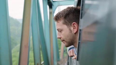 Young man looking out the train window while train cross the river over bridge Stock Footage 251004350