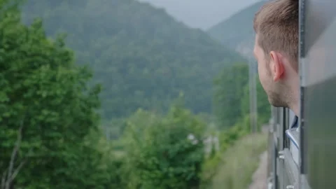 Young man looking out of train window while traveling by railway through Balkans Stock Footage 256094108