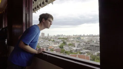 Young Man Looking Out Window With City in Background - 2 Angles Stock Footage 94759216