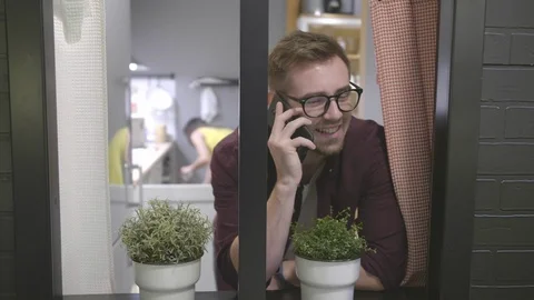 Young man looking out of window and talking on phone at home Stock Footage 125741810