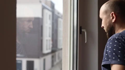 Young man looking out the window and closing the window shutter Video stock 242719855