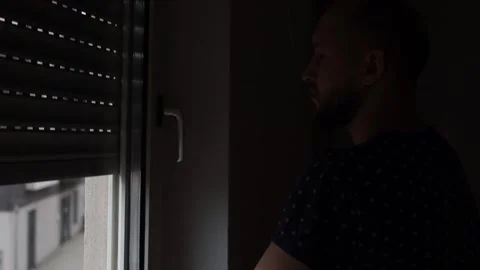 Young man looking out the window and closing the window shutter Stock-Footage 242719923