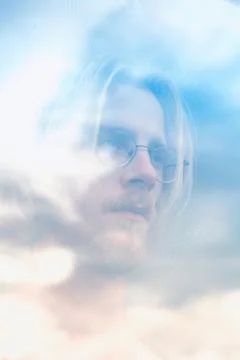 Young man looking out of window with reflection of sky Stock Photos