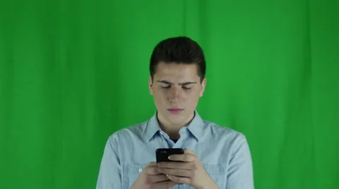 Young man is looking at phone annoyed in front of a greenscreen Stock Footage 59083588