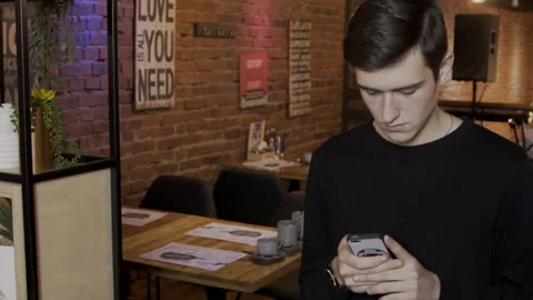 Young man is looking at phone screen while standing in cafe. Stock Footage 85713216