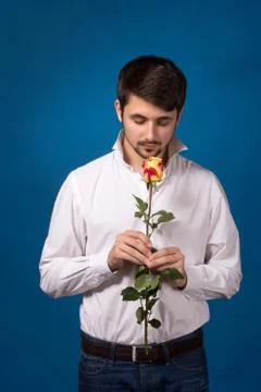 Young man looking to red rose on blue background Fotos de archivo