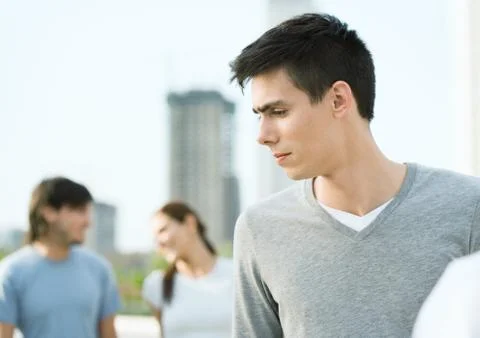 Young man looking to the side, young couple in background Stock Photos