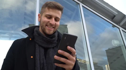 A young man is looking at a smartphone. A man looks at the phone and smiles. Stock Footage 119201068