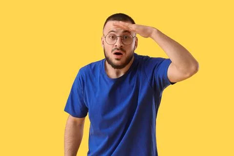Young man looking at something on yellow background. Search concept Stock Photos