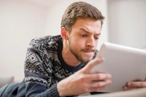 Young man looking at a tablet computer while lying on the couch. Stock Photos