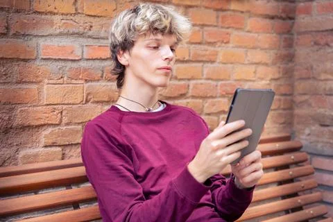 Young Man Looking Thoughtfully at a Tablet While Sitting Outdoors Stock Photos