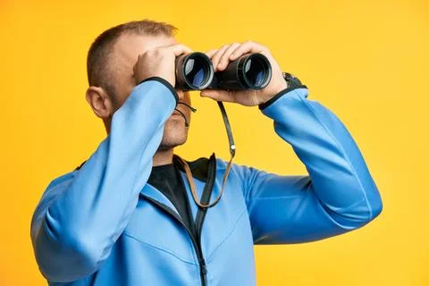 Young man looking through binoculars isolated over yellow background Stock-Fotos