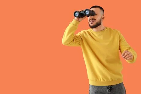 Young man looking through binoculars on orange background. Search concept Stock Photos