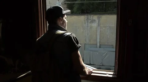 A young man looking through a window in the sun. gray wall in front Stock Footage 51757045