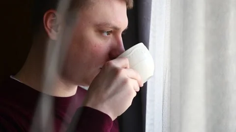 Young man looking through the window and drinking coffee. Stock Footage 61281854