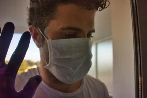 Young man looking throw the windows with protection white mask and purple glo Stock Photos