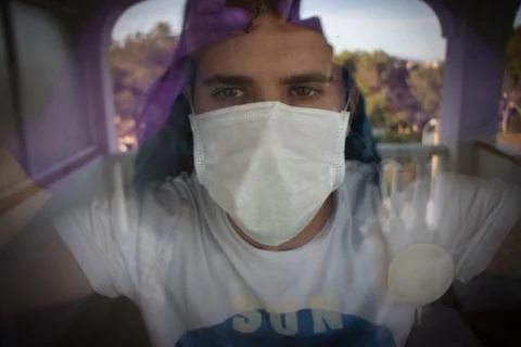Young man looking throw the windows with protection white mask and purple glo Stock Photos