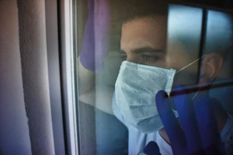 Young man looking throw the windows with protection white mask and purple glo Stock Photos