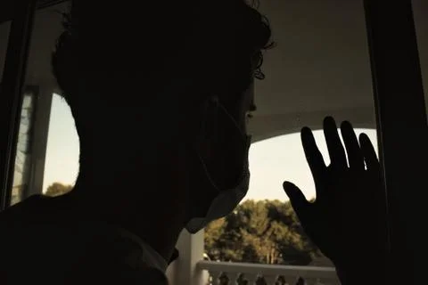 Young man looking throw the windows with protection white mask and purple glo Stock Photos