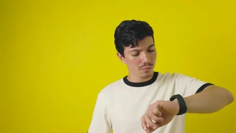Young man looking at the time worriedly on a yellow background Stock Footage 312234930