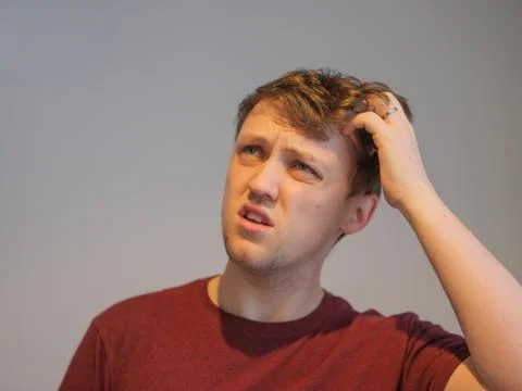A young man looking very confused and scratching his head Stock Photos
