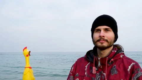 Young man looking at yellow rubber chicken by the sea. Surprised, funny emotion. Stock Footage 151045623