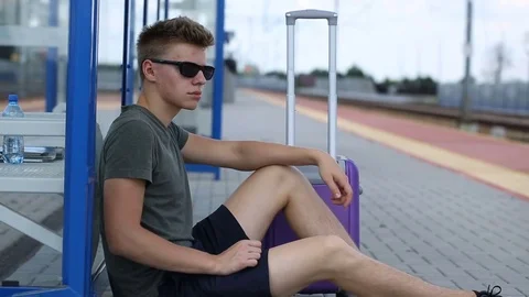 Young man looks calm while sitting on the platform and waiting for his train Stock Footage 78654386
